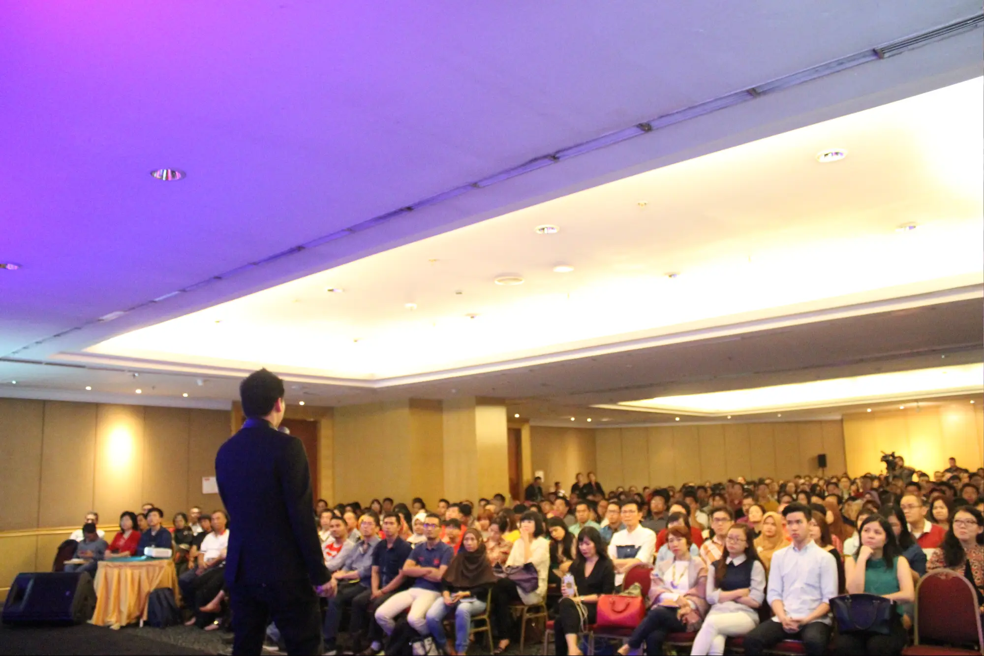Aula seminar besar dengan ratusan peserta dan lampu panggung ungu